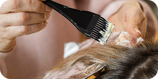 Aplicación de tinte o tratamiento capilar con brocha sobre el cabello seccionado y protegido con papel de aluminio, mostrando un proceso técnico y cuidadoso de coloración profesional.