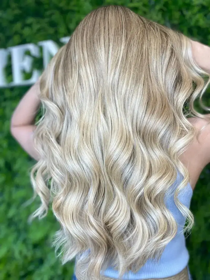 El cabello que se muestra en la imagen tiene un acabado de ondas suaves y naturales, con un color rubio brillante y vibrante que da una sensación de frescura y luminosidad. El movimiento fluido del cabello le da un toque elegante pero relajado, ideal para un look versátil que puede ser usado tanto en ocasiones cotidianas como especiales.