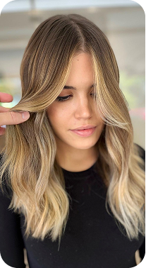 La imagen muestra un corte de cabello medio con ondas suaves, con un contraste de tonos rubios y un degradado sutil hacia las puntas. El estilo tiene un aire natural y desenfadado, con una textura suave que aporta volumen y movimiento. Las capas y los reflejos en la parte frontal enmarcan el rostro de manera favorecedora, creando un look fresco, luminoso y lleno de vida. Es un estilo perfecto para quienes buscan un toque de sofisticación sin perder la naturalidad.