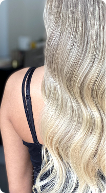 Para el texto alternativo de esta imagen, te sugiero lo siguiente: "Vista posterior de una persona con el cabello largo, rubio y ondulado, mostrando un acabado brillante y saludable."