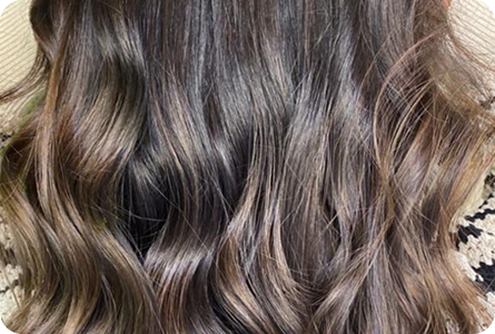 La imagen muestra una vista posterior de un cabello largo, con ondas suaves y brillantes, mostrando una mezcla de tonos oscuros y claros. La textura del cabello es ligera, con un acabado natural y bien cuidado.